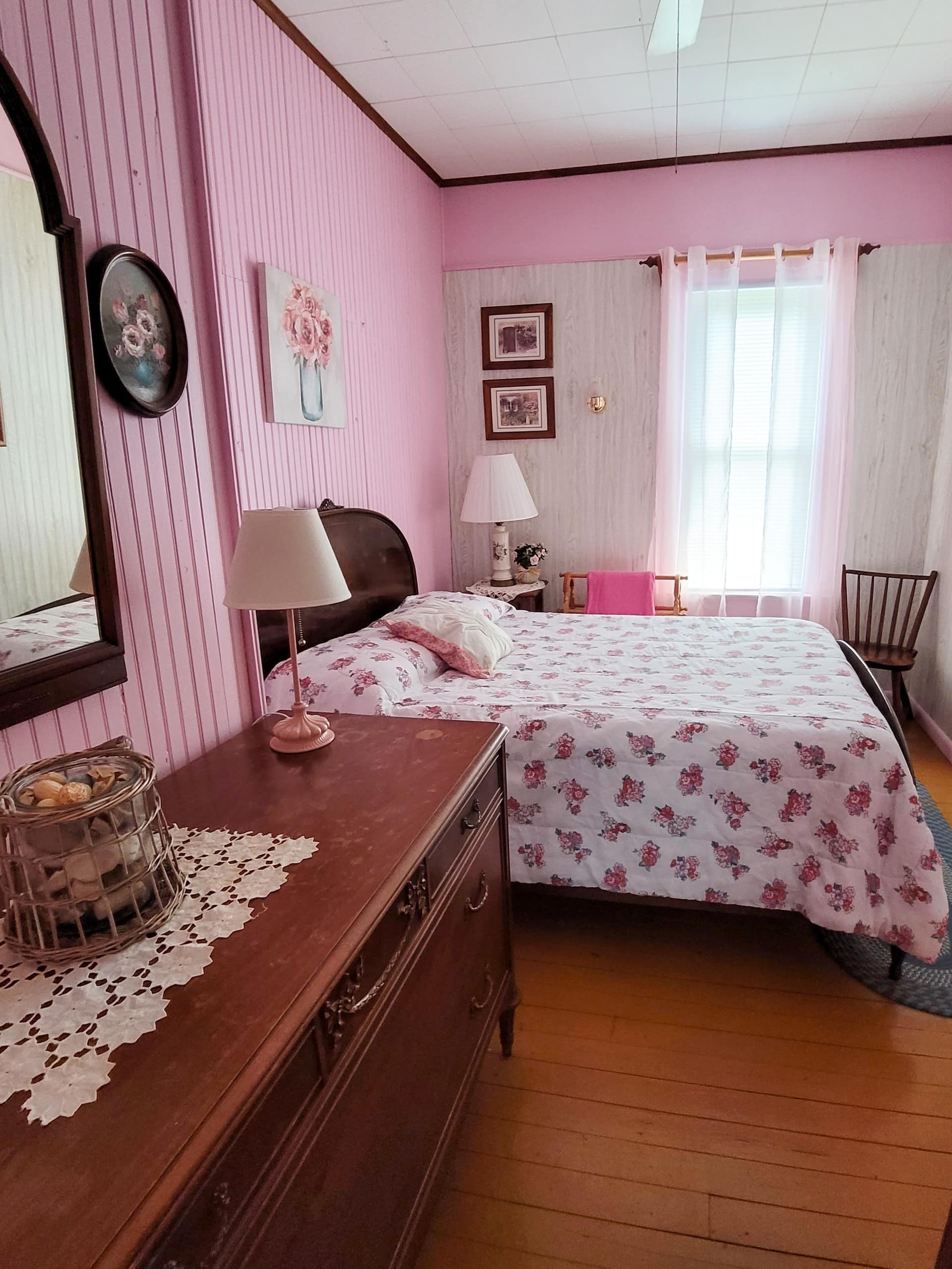 Bedroom with rose walls, a wooden dresser and a made bed